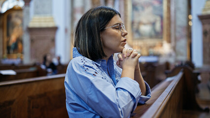 Young beautiful hispanic woman praying on a church bench at St. Karl BorromÃ¤us church