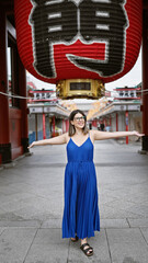 Joyful hispanic woman in glasses, with arms open, looking around senso-ji temple, tokyo with a beautiful smile embracing the carefree lifestyle.