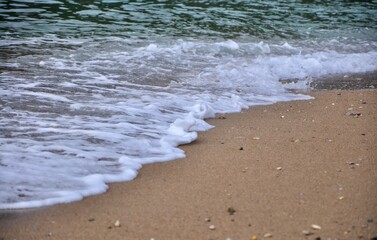 Sea sandy shore with an oncoming foam wave. Travel and tourism. Natural summer background. A foaming wave comes to the sand beach like a high tide