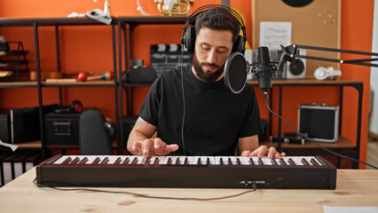 Young hispanic man musician playing piano singing song at music studio