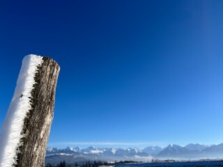 Closeup of wooden fence post with snow on one side, deep blue sky in the background