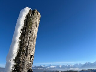 Closeup of wooden fence post with snow on one side, deep blue sky in the background