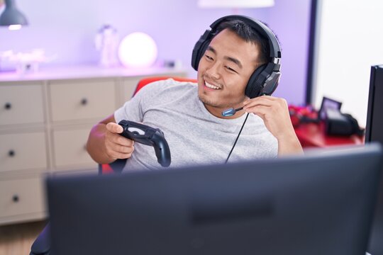 Young chinese man streamer playing video game using joystick at gaming room