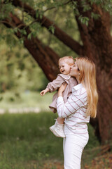 Fototapeta premium A joyful image of a mother and child in a park, mother is holding the child up in the air and smiling. Family in casual clothes with copy space. Concept happiness, family, or childhood.