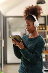 Fototapeta na wymiar Focused young woman interacting with a tablet while wearing headphones, engaged in digital media inside a bright room..