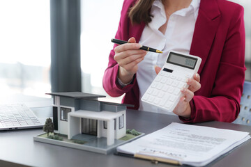 Real estate professional with pen and calculator in hand, analyzing costs beside an architectural model of a house..