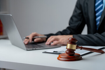 Legal professional in suit typing on a laptop with a judge's gavel in the foreground, symbolizing law and justice..