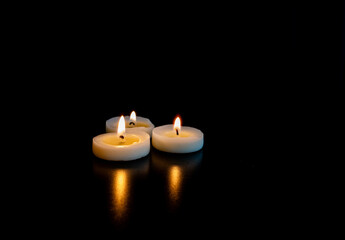 Obraz na płótnie Canvas trois petite bougies regroupées allumées sur une table avec un fond noir et de l'espace vide