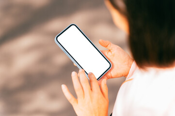 View from above of a blank phone screen held by female hands outdoors on a sunny day.