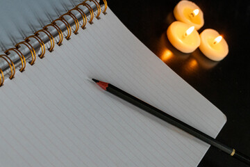 Cahier à spirale ouvert sur une page blanche avec un crayon sur une table noire avec trois petites...