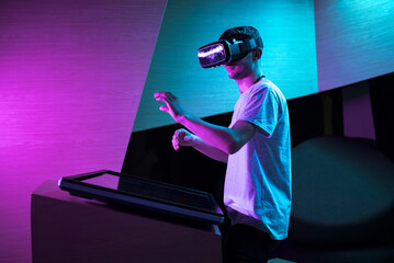 Young man interacting in a digital world, using virtual reality headset with motion tracking tech, making hand gestures in the air.