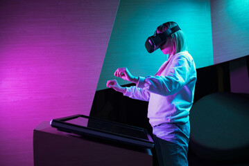 Girl in a virtual reality headset standing in front of a touch screen display making hand gestures in the air. Hand tracking concept. - obrazy, fototapety, plakaty