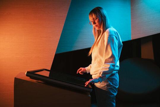 Adolescent girl using touch screen display, skillfully searching interactive content on the modern museum exhibition. Digital technology concept.