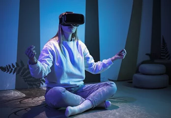 Fotobehang Girl wearing a virtual reality headset sitting in a lotus pose and meditating in a room with blue neon light and glowing neon lines. © 24K-Production