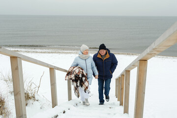 An elderly couple climbs a wooden staircase in winter by the sea