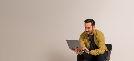 Confident young businessman working over laptop while sitting on chair against white background