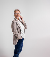 Elderly female professional talking over mobile phone and smiling at camera over white background