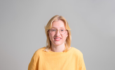 Portrait of confused businesswoman with blond hair and eyeglasses making face on white background