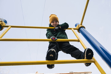 happy child kid boy climbs on the horizontal bars on the playground in the park in autumn