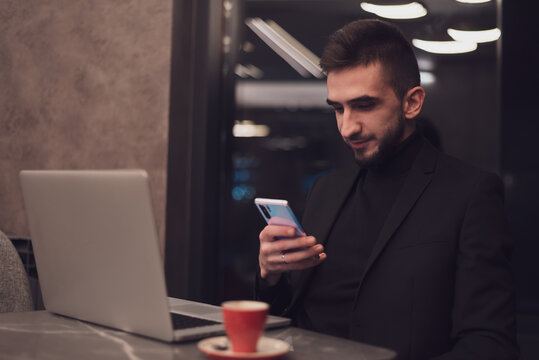 Young business man using a smartphone while working at his office during the night.