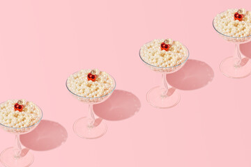 Creative concept of a creamy dessert in a tall elegant glass with a cherry on top, retro style, candy pink background.