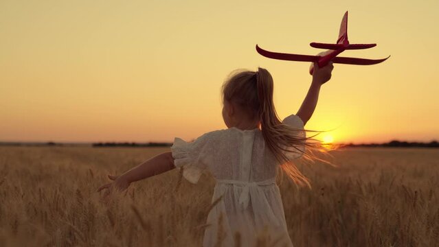 Child girl plays with toy airplane on field, kid fly into future. Kid aviator girl wants to become pilot astronaut. Slow motion. Kid play with toy airplane. Little girl dream of flying, becoming pilot