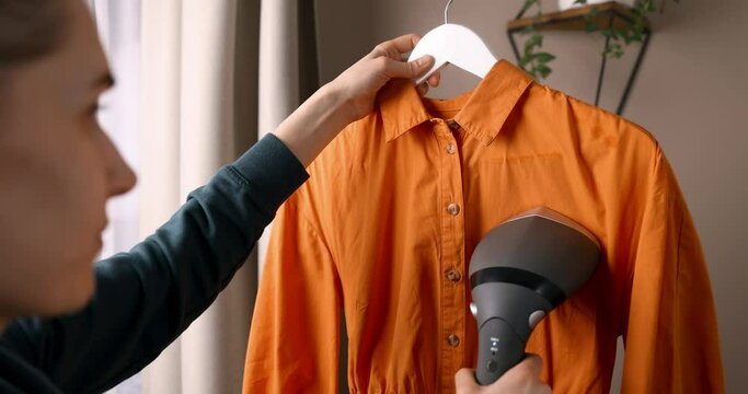 woman ironing shirt with electric clothes steamer at home