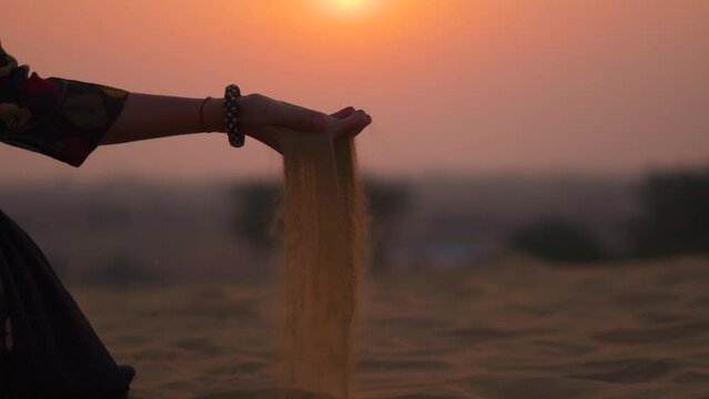 Close-Up Shot Of Sand Falling From Woman Hand during Sunset at Thar desert in Jaisalmer, Rajasthan, India. Female pouring sand in the desert. Women grabbing fine desert sand during sunset.