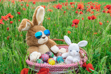 Lapin en peluche au milieu d'un champs de coquelicots avec un panier en osier rempli d'œufs de Pâques décorés.	