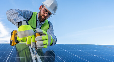 portrait of an engineer installing and giving maintenance to solar panels using a drill, professional technician working on a roof with blue sky background with copy space for text