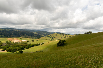 Fototapeta na wymiar Panoramic view of the Lagoon Valley Park in Vacaville, California, USA, featuring the chaparral with green grass and spotty light and cloudy sky copy space