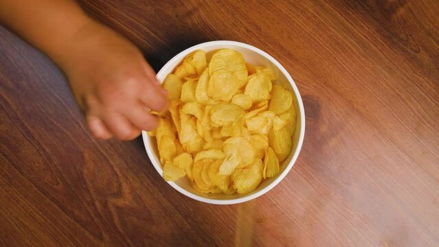 potato chips, Many people use their hands to take potato chips from the white bowl on brown wooden table, Time Lapse and top view shot