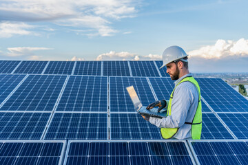 professional engineer using a laptop in front of a solar panel power station, handsome male technician electrician looking at the screen holding a computer