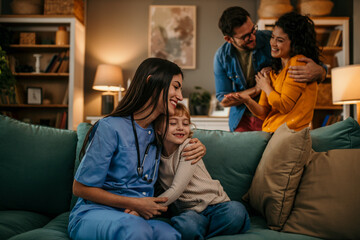 Loving parents look on with smiles as a home nurse shares a tender hug with their kid