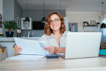 Beautiful middle-aged woman in glasses smiling at camera. She does Quarterly financial reports at...