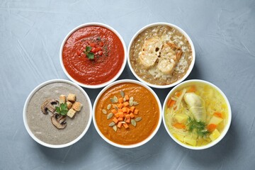 Tasty broth and different cream soups in bowls on gray table, flat lay