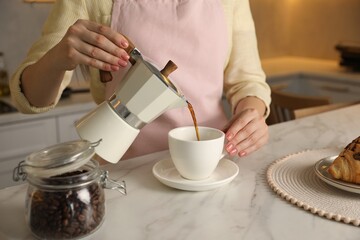Fototapeta na wymiar Woman pouring aromatic coffee from moka pot into cup at white marble table, closeup