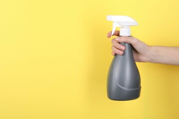 Woman holding plastic spray bottle on yellow background, closeup. Space for text