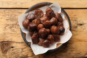 Roasted edible sweet chestnuts in bowl on wooden table, top view