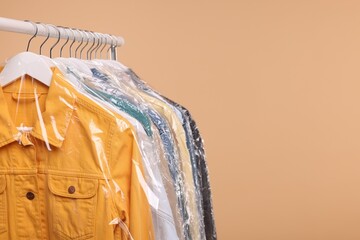 Dry-cleaning service. Many different clothes in plastic bags hanging on rack against beige...