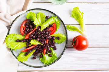 Appetizing black beans, tomatoes and lettuce on a plate on the table top view