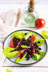 Vegetarian salad of black beans, tomatoes and lettuce on a plate vertical view