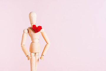 Wooden man with a red origami heart on his chest on a pink background