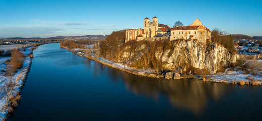 Tyniec near Krakow, Poland. Benedictine abbey and monastery on the rocky cliff and its water reflection in Vistula River. Wide aerial Panorama in winter in sunset light - obrazy, fototapety, plakaty