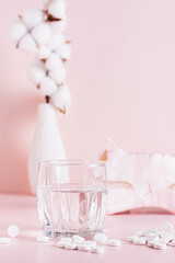 Sleeping pills, a glass of water and a sleep mask on a pink background  vertical view