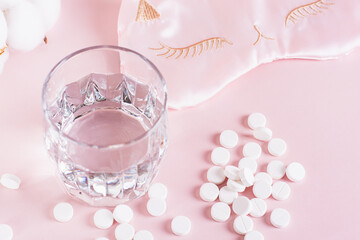 Good sleep concept, sleeping pills, glass of water and sleep mask on pink background