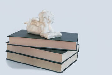 White Angel, a sculpture of an angel reading a book, lies on three books with green covers, a...