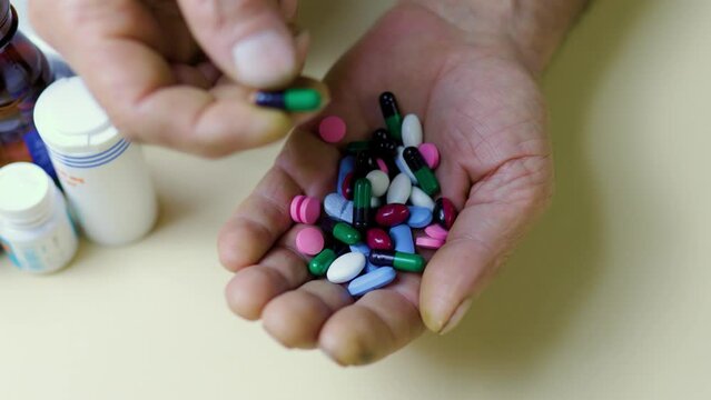 Unrecognizable close up handful of pills in his hand, other hand takes one piper from common pile.