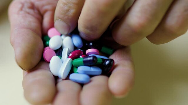 Blurred, selective focus, multicolored tablets in senile palm of human unrecognizable.