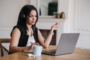Professional woman in headphones at laptop in virtual meeting, explaining concept